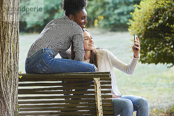 Lächelnde junge Freunde machen ein Selfie mit ihrem Smartphone in einem öffentlichen Park