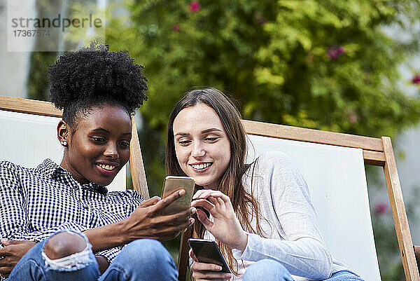 Lächelnde junge Freunde benutzen Smartphones im Park