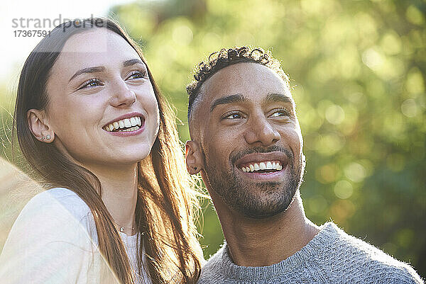 Nahaufnahme eines lächelnden jungen Paares  das in einem öffentlichen Park wegschaut
