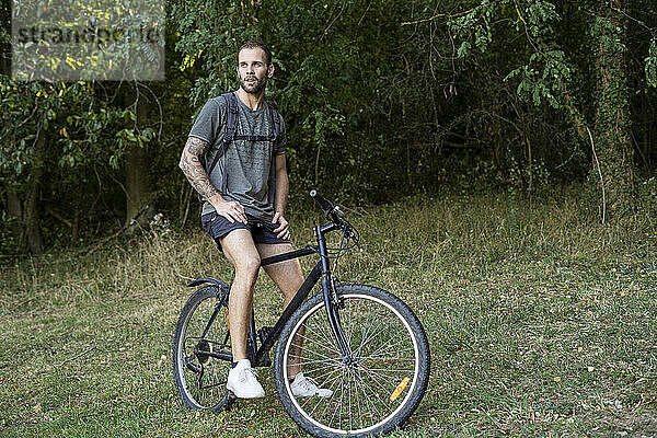 Nachdenklicher junger Mann sitzt auf einem Fahrrad im Wald