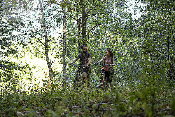 Lächelndes junges Paar geht mit Fahrrädern im Wald spazieren