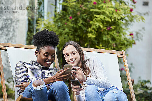 Lächelnde junge Freunde benutzen Smartphones im Park