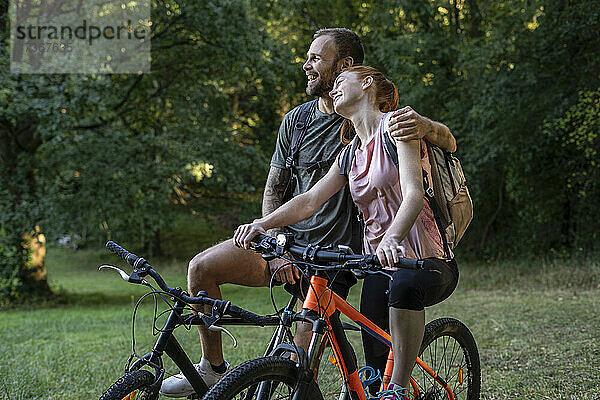 Lächelndes junges Paar sitzt auf Fahrrädern im Wald