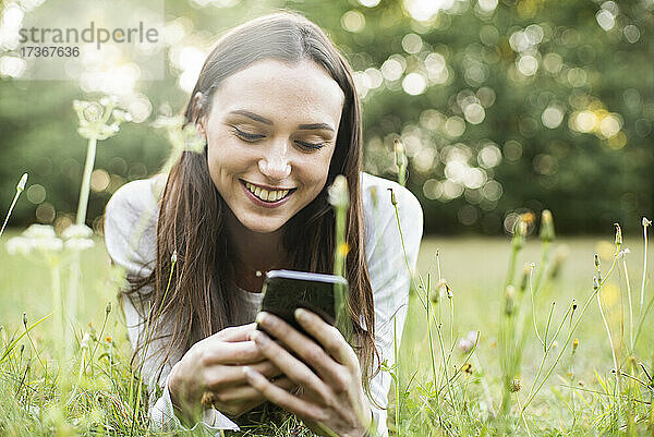 Junge Frau benutzt ihr Smartphone  während sie im Park liegt