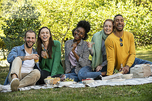 Porträt von lächelnden jungen Freunden beim Picknick im öffentlichen Park