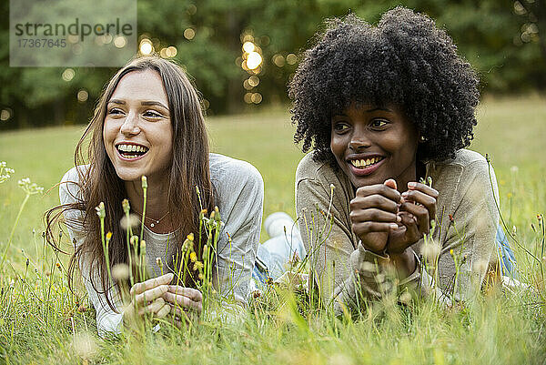 Lächelnde junge Freundinnen liegen im Park