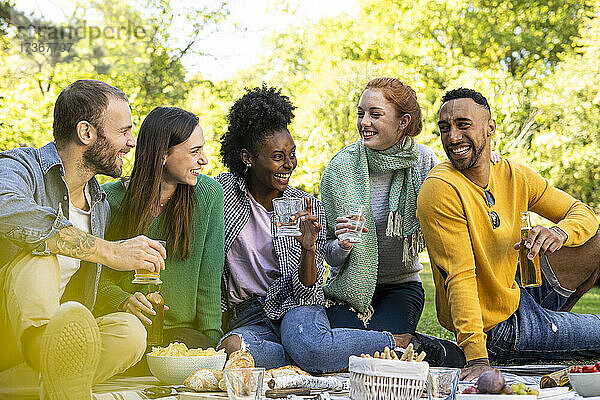 Lächelnde junge Freunde sitzen zusammen in einem öffentlichen Park