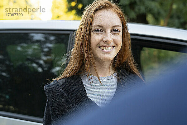 Lächelnde junge Frau  die vor einem Auto steht