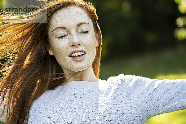 Nahaufnahme einer lächelnden jungen Frau mit geschlossenen Augen im Park