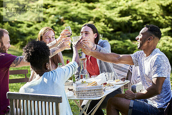 Fröhliche junge Freunde stoßen mit Getränken im Garten an