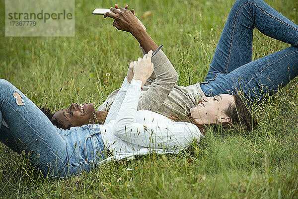 Junge Freundinnen liegen im Gras und benutzen ein Smartphone im Park