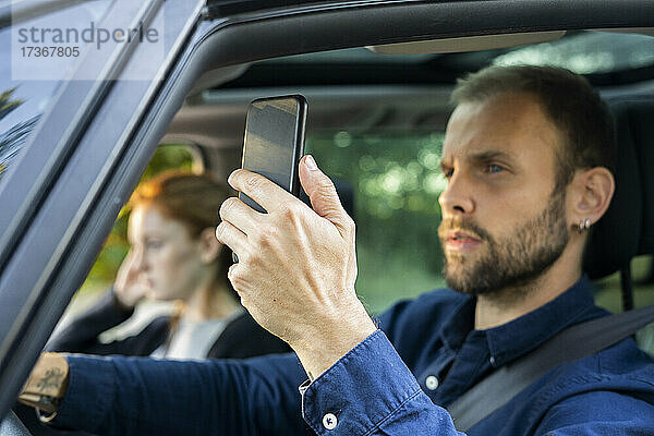 Junger Mann benutzt Smartphone beim Autofahren