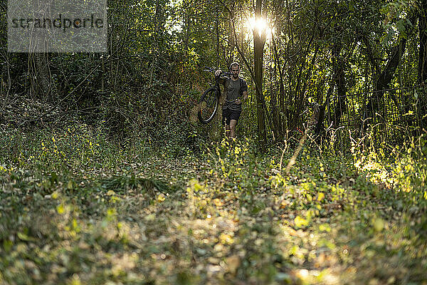 Junger Mann mit Fahrrad beim Spaziergang im Wald