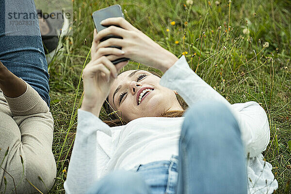 Junge Freundinnen liegen im Gras und benutzen ein Smartphone im Park