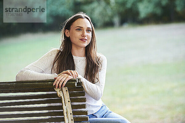 Lächelnde junge Frau sitzt auf einer Bank im Park