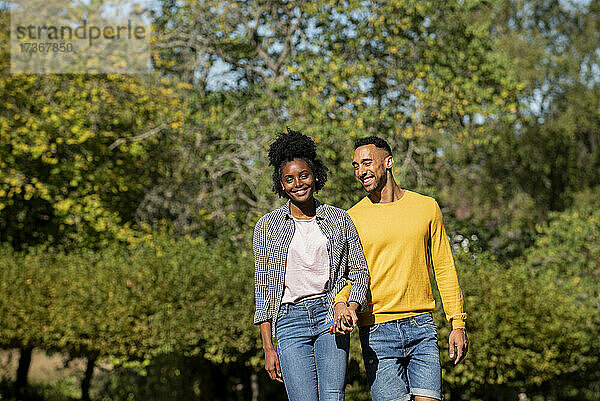 Lächelndes junges Paar mit Händchenhalten im öffentlichen Park