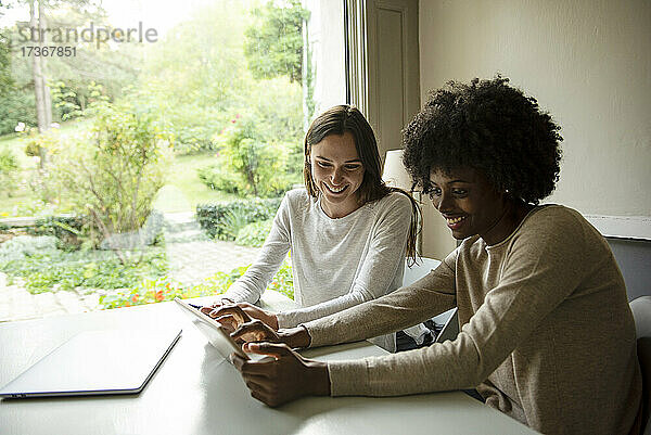 Lächelnde junge Frauen  die zu Hause ein digitales Tablet benutzen