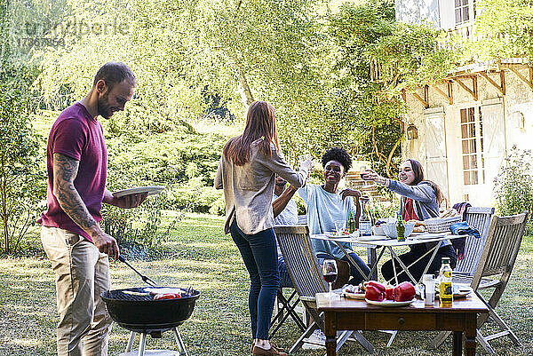 Junger Mann bereitet mit seinen Freunden am Tisch sitzend das Essen für den Grill vor