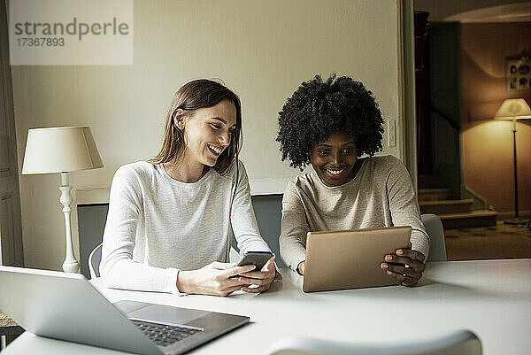 Lächelnde junge Frauen  die zu Hause ein digitales Tablet und ein Smartphone benutzen