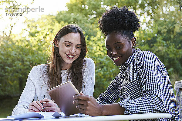 Lächelnde junge Freunde  die ein digitales Tablet benutzen  während sie im Park lernen  Orgeval