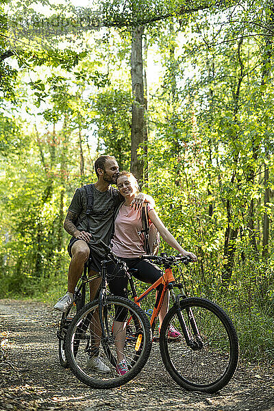 Junger Mann küsst Frau auf den Kopf  während er mit Fahrrädern im Wald steht