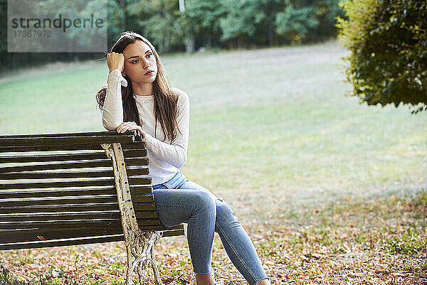 Nachdenkliche junge Frau sitzt auf einer Bank im Park