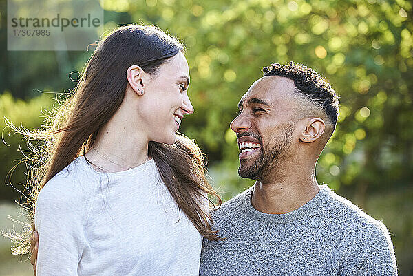 Lächelndes junges Paar  das sich im öffentlichen Park ansieht