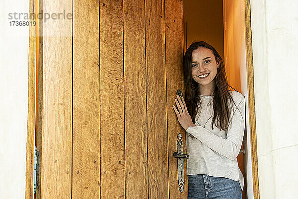 Porträt einer lächelnden jungen Frau  die in der Nähe einer Tür steht