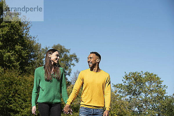 Lächelndes junges Paar beim Spaziergang in einem öffentlichen Park