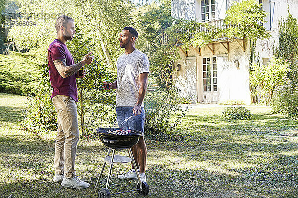 Junge Männer mit Bierflaschen unterhalten sich in der Nähe eines Grills