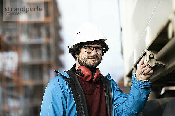 Junger Ingenieur mit Helm und Hörschutz an einer Arbeitstelle außen auf einer Baustelle  Freiburg  Baden-Württemberg  Deutschland  Europa