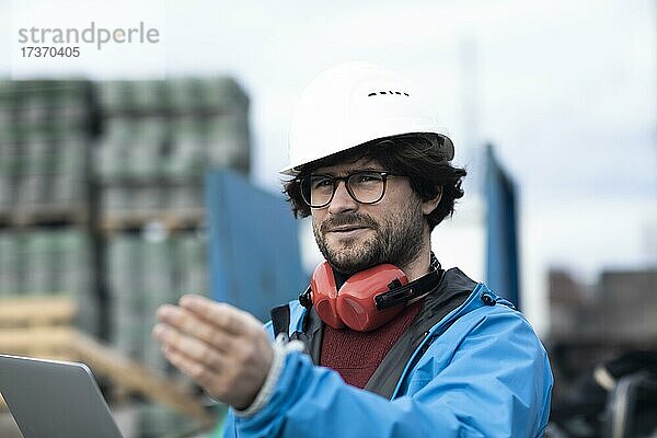 Junger Ingenieur mit Helm und Hörschutz an einer Arbeitstelle außen auf einer Baustelle mit Laptop  Freiburg  Baden-Württemberg  Deutschland  Europa