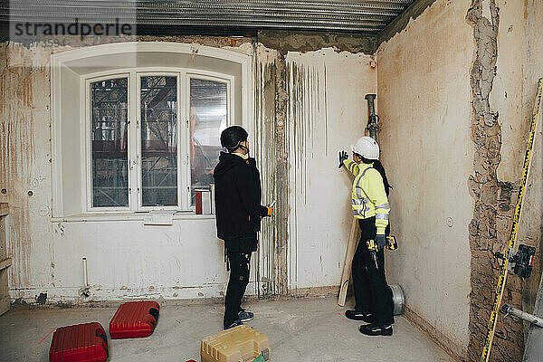 Weibliche Bauunternehmerin diskutiert mit einem männlichen Arbeiter  während sie auf der Baustelle eine Wand untersucht