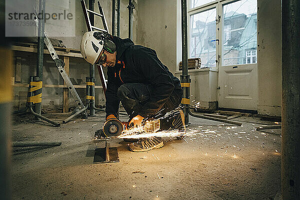 Männlicher Bauarbeiter in voller Länge bei der Verwendung einer elektrischen Säge beim Schneiden von Metall auf der Baustelle