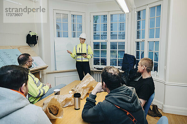 Bauunternehmerin mit digitalem Tablet diskutiert mit männlichen Kollegen bei der Planung im Büro