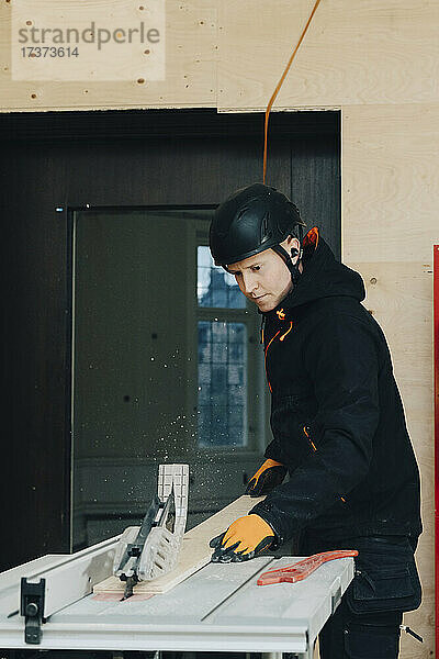 Männlicher Arbeiter benutzt eine Tischsäge zum Schneiden von Holzbrettern auf einer Baustelle