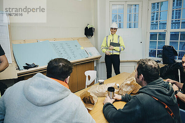 Lächelnde Ingenieurin im Gespräch mit männlichen Bauarbeitern im Büro