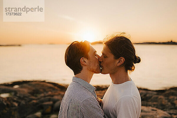 Männliche Freunde küssen sich im Urlaub am Seeufer