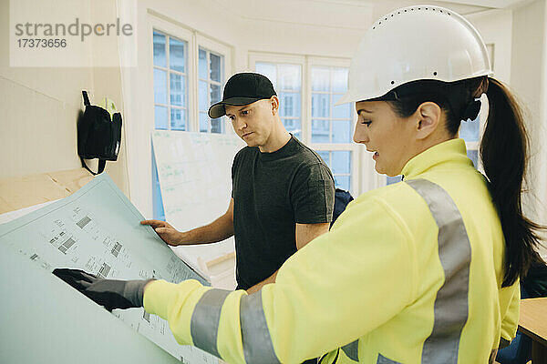 Weibliche Bauunternehmerin diskutiert mit einem männlichen Arbeiter im Büro über einen Bauplan