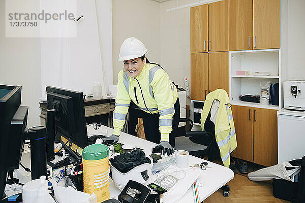 Porträt einer lächelnden Bauunternehmerin  die sich auf einen Schreibtisch im Büro stützt