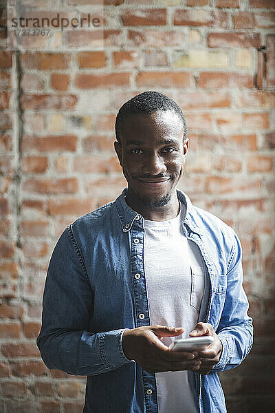 Porträt eines lächelnden männlichen Unternehmers mit Smartphone im Kreativbüro