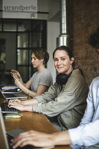 Porträt einer Hackerin  die mit Kollegen im Büro sitzt