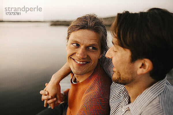 Lächelnder Mann mit Arm um seinen Freund am See