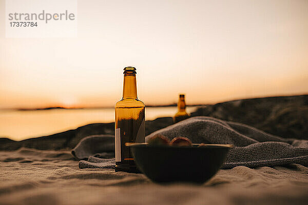 Essensschale und Bierflasche am Seeufer bei Sonnenuntergang