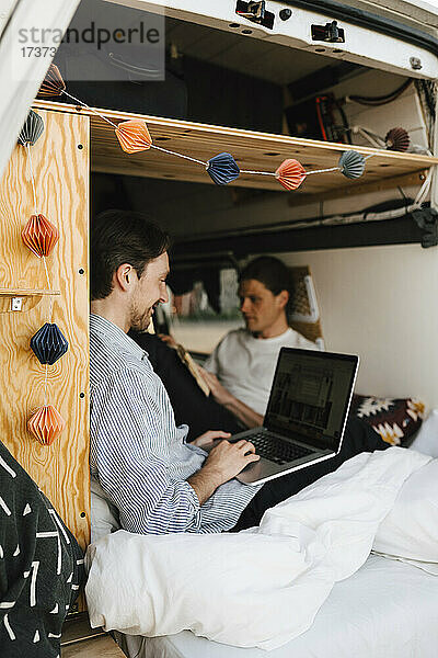 Mann mit Laptop sitzt mit Freund im Wohnmobil