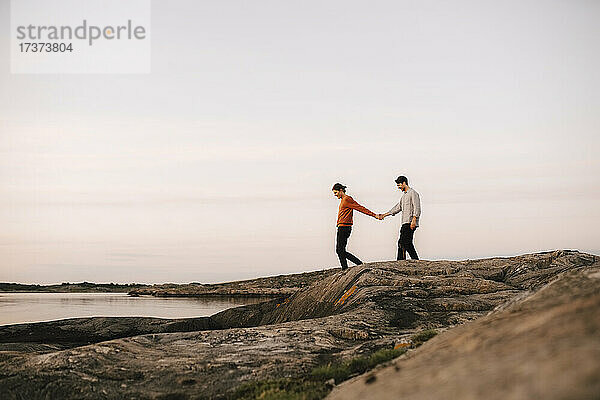 Homosexuelles Paar hält Hände beim Spaziergang am Seeufer gegen den Himmel