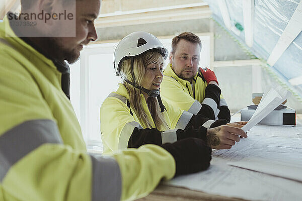 Weiblicher Bauunternehmer diskutiert mit männlichen Kollegen auf der Baustelle über den Grundriss