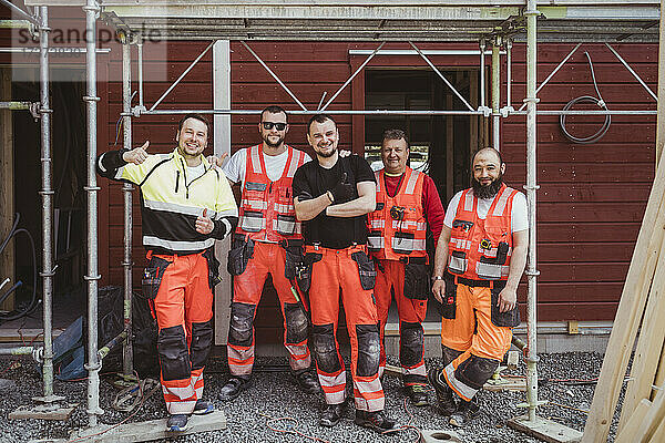Lächelnde männliche Bauarbeiter  die auf der Baustelle zusammenstehen  in voller Länge