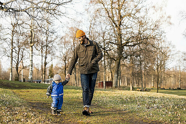 Vater und Sohn halten sich beim Spazierengehen im Park in voller Länge an den Händen