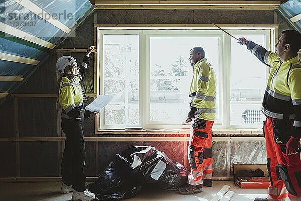 Eine Bauunternehmerin untersucht ein Fenster mit einem männlichen Bauarbeiter auf der Baustelle